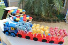 a table topped with lots of cupcakes and cake on top of it next to a train