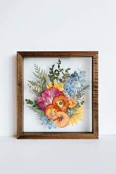 a wooden frame with flowers in it on a white wall next to a brown framed object