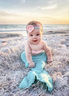 a baby sitting on the beach with a mermaid tail