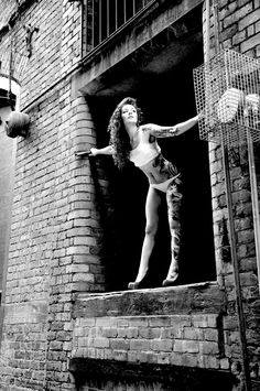 a woman standing on the ledge of a brick building with her arms outstretched and legs spread out