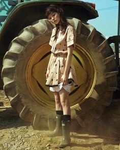 a young woman standing in front of a large tractor with her hands on her hips