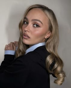 a woman with long blonde hair wearing a black shirt and blue collared shirt is looking at the camera