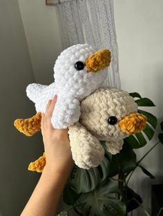 a hand holding two stuffed animals in front of a plant