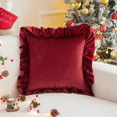 a red pillow on a white couch next to a christmas tree and other holiday decorations