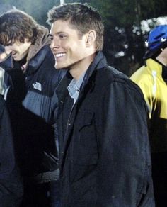 two young men standing next to each other in the snow at night, one holding his hand up