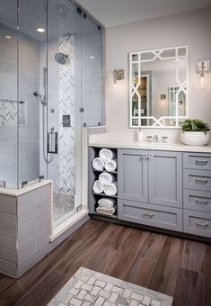 a bathroom with gray cabinets and white towels on the counter, along with a walk in shower