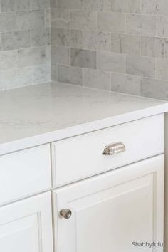 a white kitchen with marble tile backsplash and stainless steel pulls on the cabinet doors