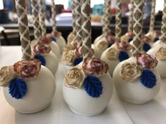 several white vases with gold and blue flowers are lined up on a table in front of candles