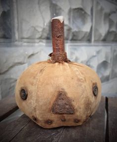 a pumpkin sitting on top of a wooden table next to a stone wall with a stick sticking out of it