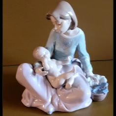 a porcelain figurine of a woman holding a baby in her lap and sitting on the ground