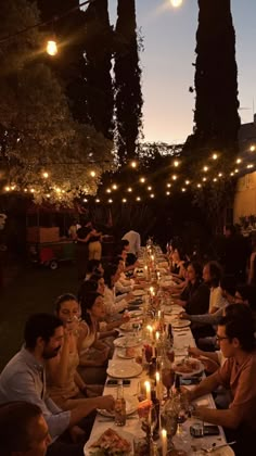 a group of people sitting at a long table with food and drinks in front of them