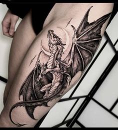 a woman's thigh with a dragon and moon tattoo design on it, in black and white