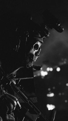 a black and white photo of a skull on a motorcycle in the dark with lights behind it