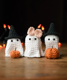 three crocheted white ghost dolls sitting next to each other on a wooden table