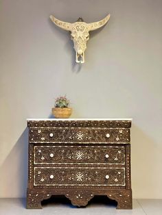 an ornate dresser with a cow's head on the wall above it and a potted plant next to it