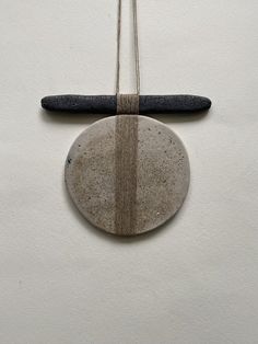 a stone hanging from a string on a white wall next to a black piece of wood