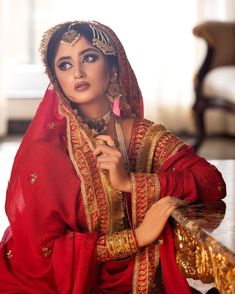 a woman in a red and gold outfit sitting on a table with her hands crossed