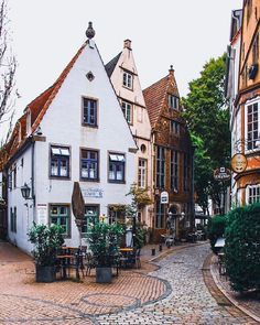 a cobblestone street with tables and chairs in front of white buildings on either side