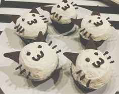 four cupcakes with white frosting and black decorations