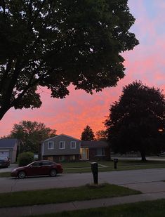 a red car is parked on the street in front of some houses and trees at sunset