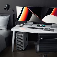 a computer desk with two monitors and a keyboard on it in front of a bed