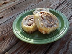 two cinnamon rolls on a green plate sitting on a wooden table next to a cup of coffee