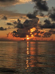 the sun is setting over the ocean with clouds in the sky and reflecting on the water