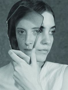 a black and white photo of a woman holding her hand to her face, looking through the mirror