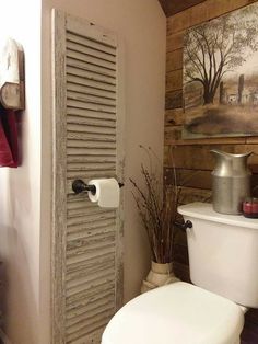 a toilet sitting next to a wooden wall with shutters on the side and a painting behind it