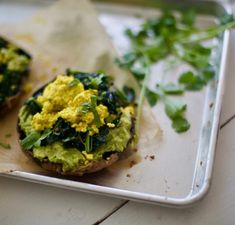 two open faced sandwiches on a tray with greens