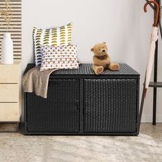 a teddy bear sitting on top of a wicker storage unit next to a coat rack