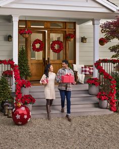 a man and woman standing in front of a house with christmas decorations on the porch