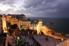 people are standing on the edge of a cliff overlooking the ocean and buildings at dusk