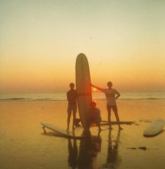 three people standing on the beach with their surfboards