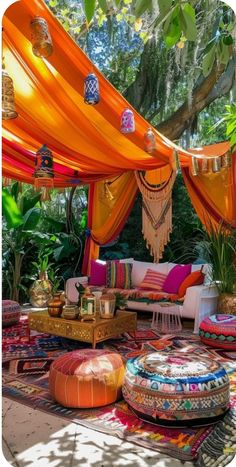 an outdoor area with lots of colorful furniture and pillows on the ground, surrounded by greenery