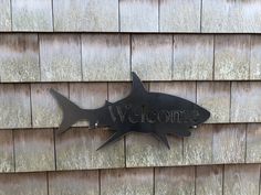 a welcome sign on the side of a wooden building with a metal shark decoration hanging from it's side