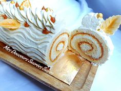 a roll cake with icing and nuts on it sitting on top of a wooden cutting board