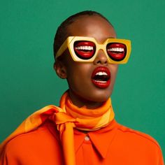 a woman with red lips and yellow glasses on her face, wearing an orange shirt