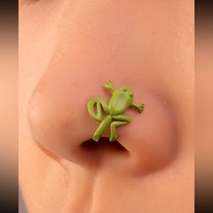 a green toy frog sitting on the side of a woman's breast with it's eyes closed