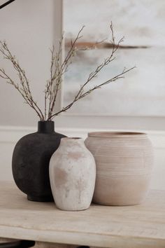 two vases sitting on top of a wooden table next to each other with branches in them