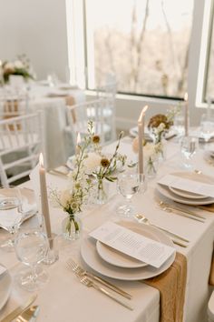 the table is set with white plates and silverware, candles, and flower centerpieces