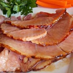 sliced ham sitting on top of a white plate next to carrots and parsley