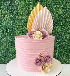 a pink and gold cake with paper flowers on top, sitting in front of a green wall