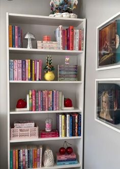 a white book shelf filled with books next to two pictures on the wall behind it