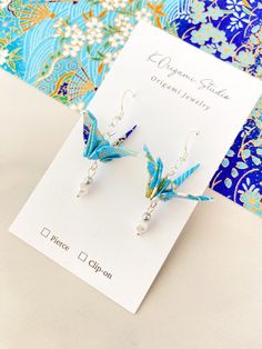 the origami crane earrings are on display in front of a blue and white background