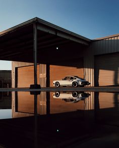 a white car parked in front of a building next to a body of water with its reflection on the ground