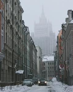 cars driving down a snowy city street in front of tall buildings with spires on top