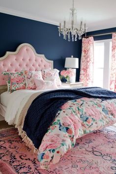 a pink and blue bedroom with floral bedding, chandelier, rugs and curtains