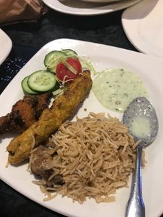 a white plate topped with meat and veggies next to rice on a table