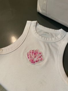 a white tank top with pink sequins on the front and back, sitting on a table